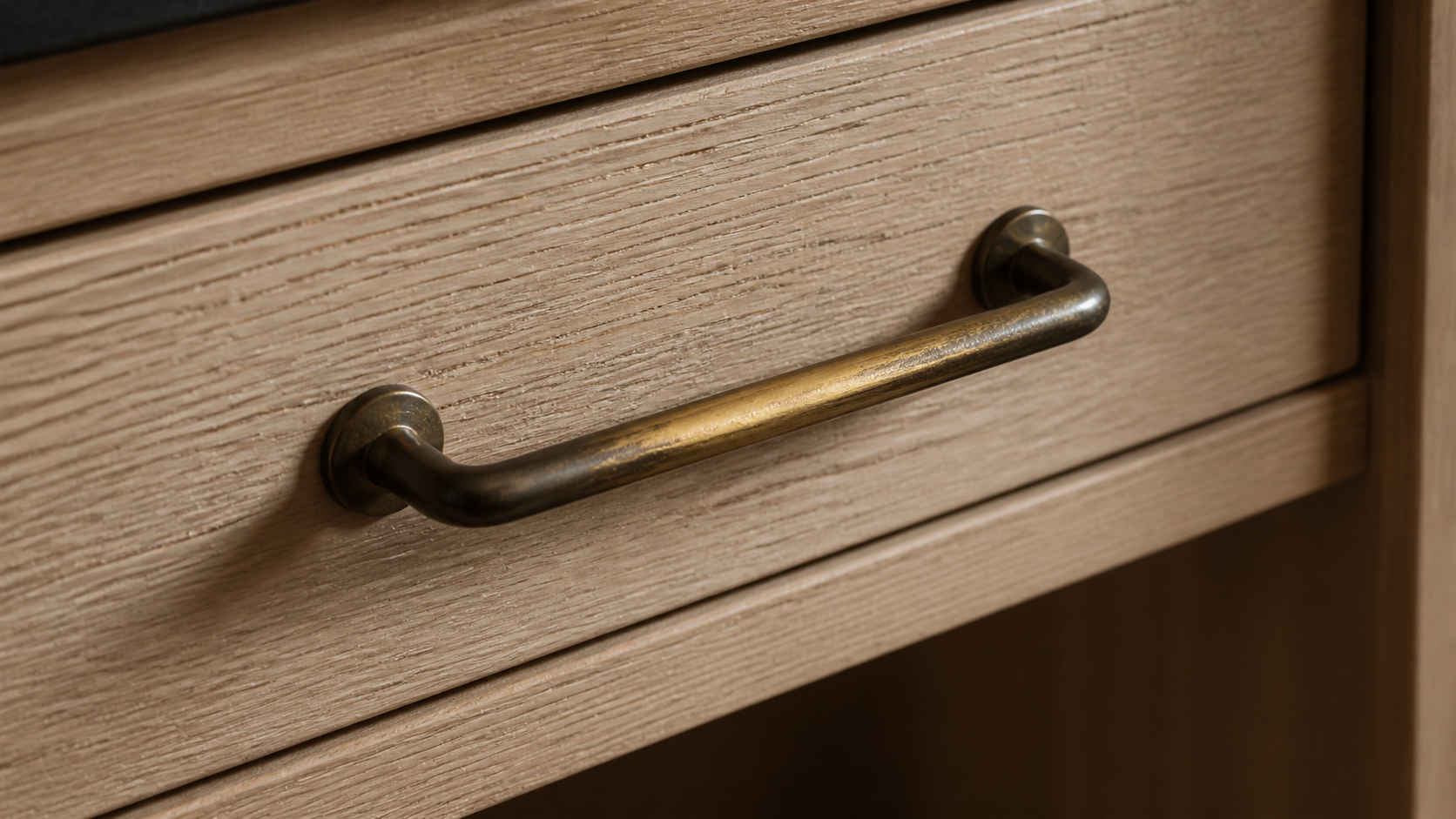 Unlacquered brass cabinet pull with hand-worn patina on a white oak drawer