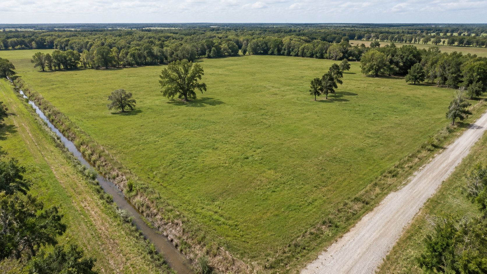 Aerial view of a cleared acreage lot bordered by a drainage ditch and gravel drive